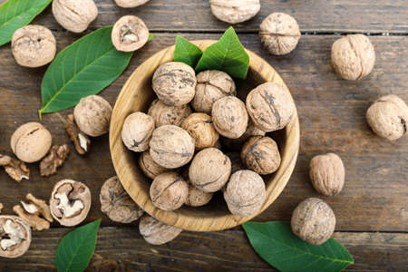Walnuts harvest with leaves, nutritious product, nuts in a plate and scattered on the table
