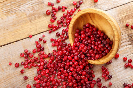 Cranberries in a plate and scattered on a wooden background. Cooking cranberry jamの写真素材
