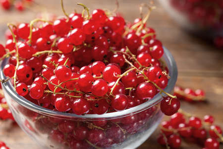 Red currant in a glass plate on a wooden background, cooking a healthy dish of red currant, close-up