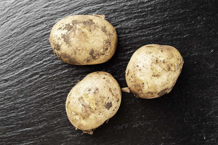 Young unwashed potatoes scattered on a black background, space for textの写真素材