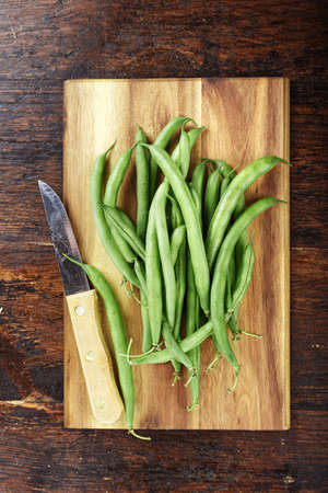 Green french beans on cutting board and dark wooden background, top view