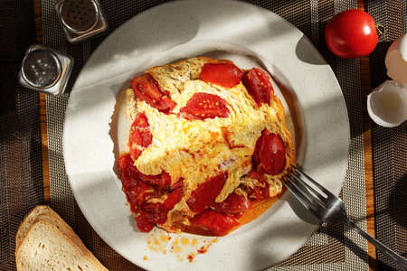 Homemade omelette with tomatoes in a plate on the table, top viewの写真素材