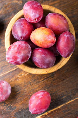 ripe plums in a wooden plate, with leaves, on a wooden backgroundの写真素材
