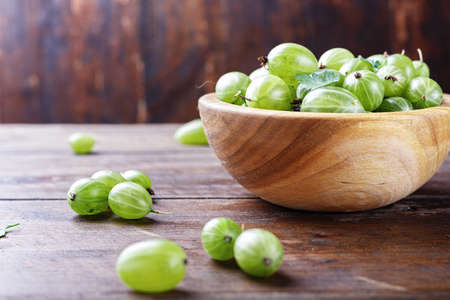 green gooseberry in a wooden plate on a wooden backgroundの写真素材