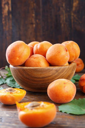 apricots summer harvest in wooden plate with green leaves, close-up, on a wooden backgroundの写真素材
