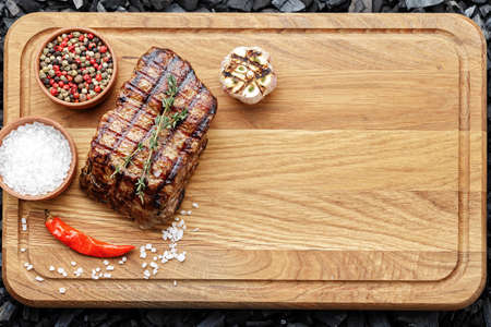 Cooked steak on a wooden cutting board with spices and a sprig of rosemaryの写真素材