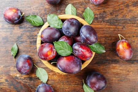 ripe plums in a wooden plate, with leaves, on a wooden backgroundの写真素材