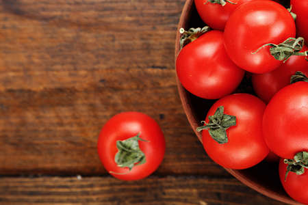 fresh cherry tomatoes in a clay plate, on a wooden background, space for textの写真素材