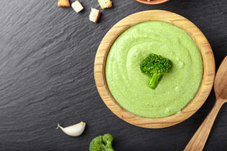 cream broccoli soup on a black slate background, next to a wooden spoon and crackers, top view. space for textの写真素材