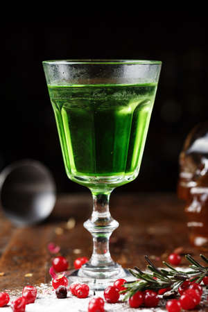 strong green alcoholic drink absinthe in a glass on the bar, beside scattered berries of cranberries
の写真素材