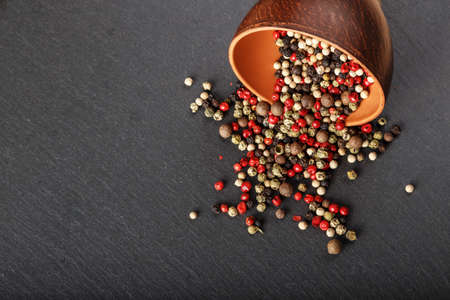 scattered multi colored pepper peas in a clay plate in the center on a black background, top view