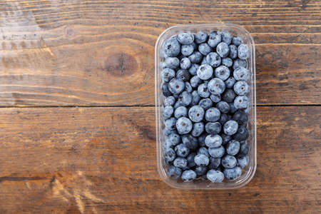 ripe organic bog whortleberry in a plastic container on a wooden backgroundの写真素材