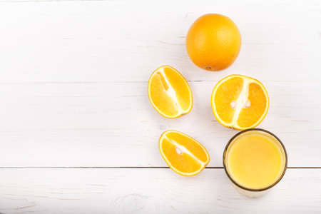 Fresh from oranges in a glass on a white background. Next to them are cut oranges. Vertical photo