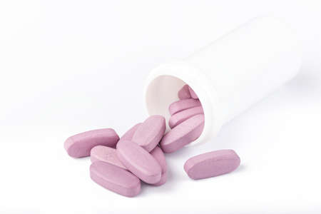 large pink pills spilled out of a plastic jar on a white background, isolated