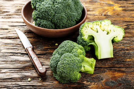 broccoli in a clay plate on a wooden table, next to a whole cabbage are cut inflorescences の写真素材