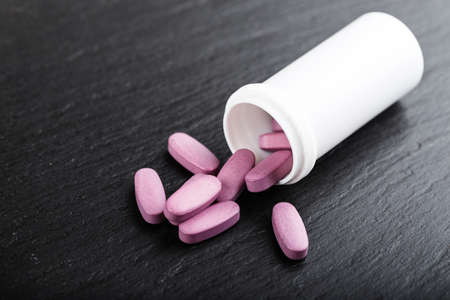 tablets are scattered from a white plastic jar and a black background, space for text