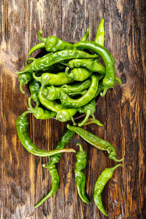 Green chili peppers placed in a clay plate on a brown wooden table.の写真素材