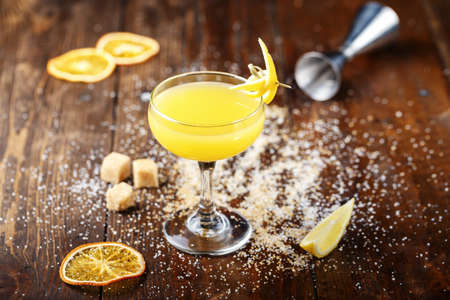 glass with yellow lemon cocktail on the bar, on a black background. the cocktail is decorated with lemon zestの写真素材