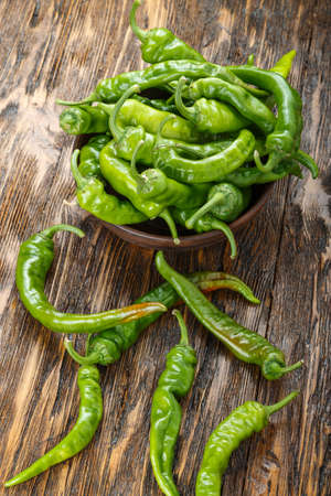 green chili peppers placed in a clay plate on a brown wooden table. with space for textの写真素材