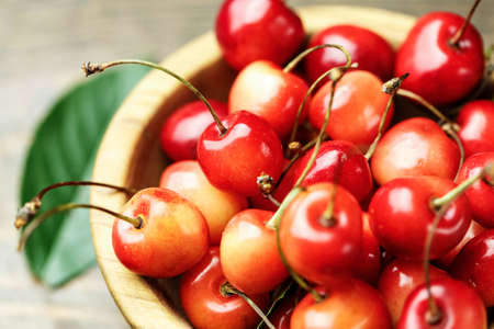 Ripe cherries with leaves on a wooden background, in a wooden plate