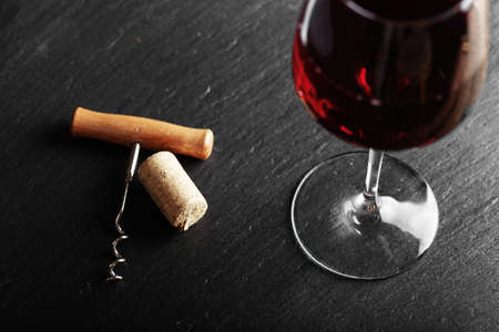 red wine in a glass, next to it lies a vintage corkscrew, on a black background, space for textの写真素材