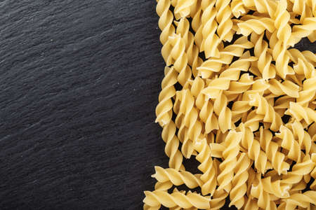 raw Italian spiral paste scattered on a black background, space for textの写真素材