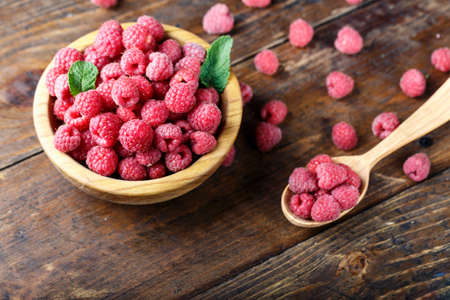 raw fresh raspberries in a spoon on a wooden background, well visible texture of berries, space for...