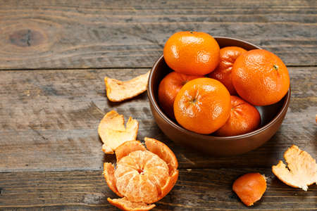 ripe whole and peeled tangerines in a plate on a wooden table