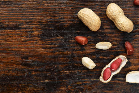 raw peanuts in a peel on a wooden background, space for text