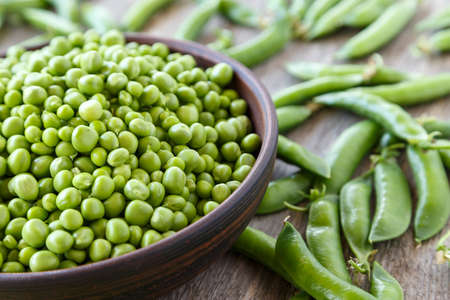 Peeled green peas in a plate on a wooden table. It lies next to pea pods. Horisontal photoの写真素材