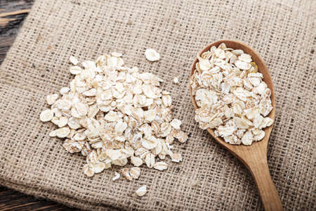 raw oat flakes in a spoon on a napkin from a sacking on a wooden table
