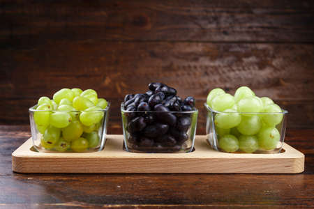 different grape varieties on a wooden background, space for text