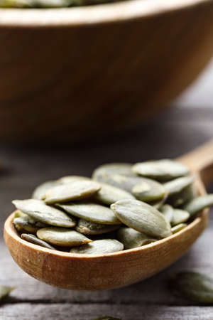 pumpkin seeds in a wooden spoon, close-up. in the background is seen a wooden plateの写真素材