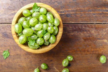ripe berries of gooseberry in a plate. harvest of berries on a wooden background. place for textの写真素材