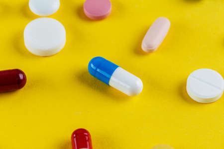 different pills and capsules scattered on a yellow background, space for text