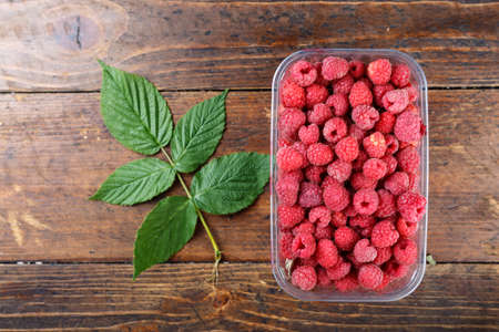 fresh raspberries in a plastic container on a wooden background, space for text