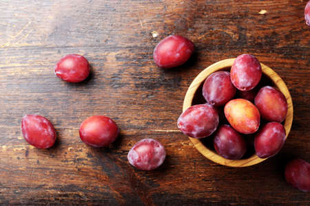 ripe plums in a wooden plate, with leaves, on a wooden background