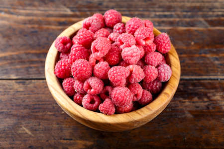 ripe raspberries on a wooden background in a wooden plate. delicious berry for making jamの写真素材