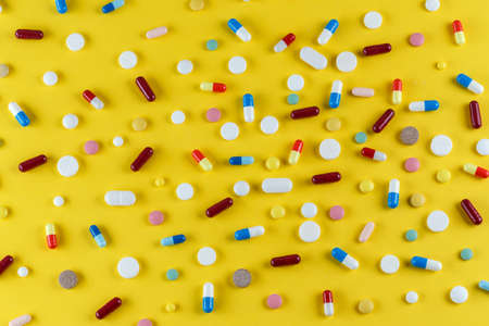 different pills and capsules scattered on a yellow background, space for textの写真素材