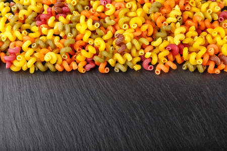 Multicolored pasta is scattered on a black slate background. place for textの写真素材