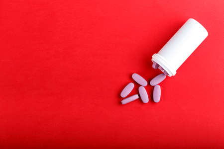 Vitamins in the form of pink long tablets are poured from a bottle, on a table on a red background