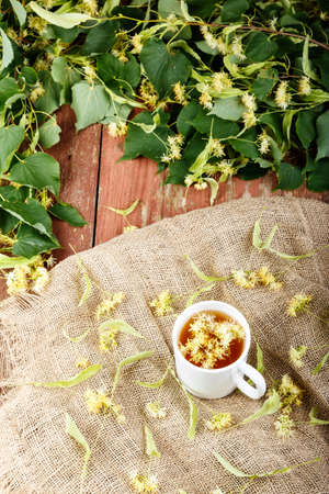 linden flowers are scattered on sackcloth. next to it is a cup of lime tea. place for textの写真素材