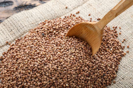 buckwheat groats scattered on a wooden table. cereal on sackcloth, near a wooden spoon. space for textの写真素材