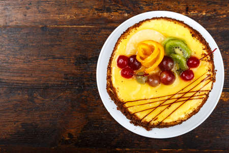 fruit cake with yellow cream, decorated with cherries and grapes, closeup