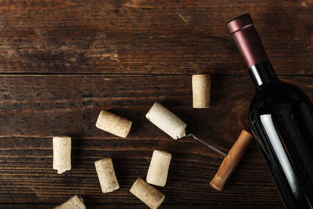 A bottle of red wine and a lot of corks on a wooden background. without labels. space for text