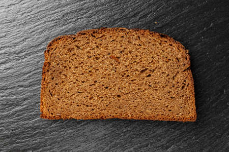 a slice of black bread on a black slate background. place for text