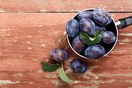 ripe plums in a shabby wooden saucepan on the table. cooking plum dessert