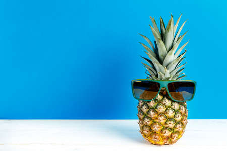whole pineapple in sunglasses on blue background. space for textの写真素材