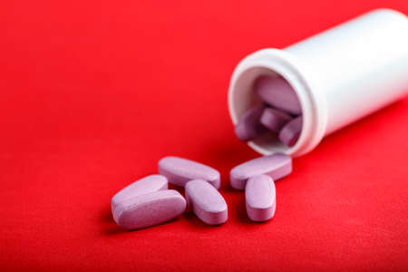 tablets poured out of a bottle on a red background. headache remedy. space for textの写真素材