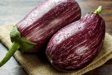 two ripe motley eggplants on a wooden table, lying on burlap. place for textの写真素材